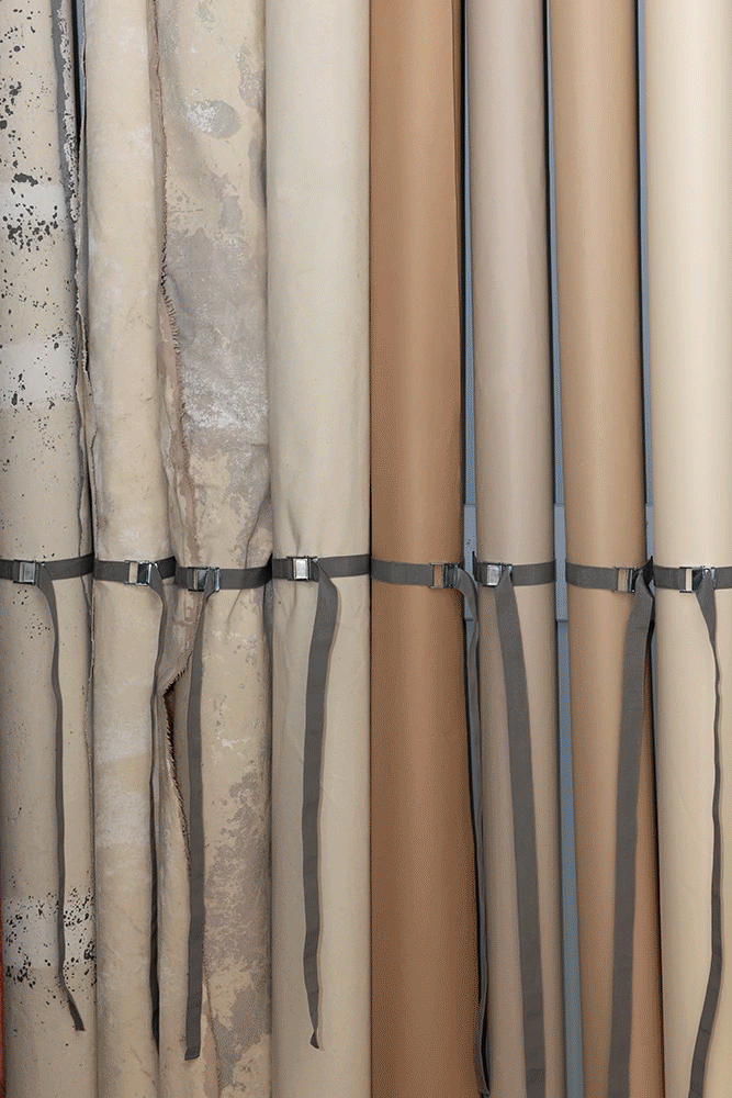 Mehrere aufgerollte Fotohintergründe in neutralen Beige-, Sand- und Brauntönen, ordentlich nebeneinander aufgehängt im Fotostudio C43 in Wien.